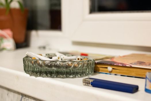 Glass ashtray with cigarette butts in sunlight close up