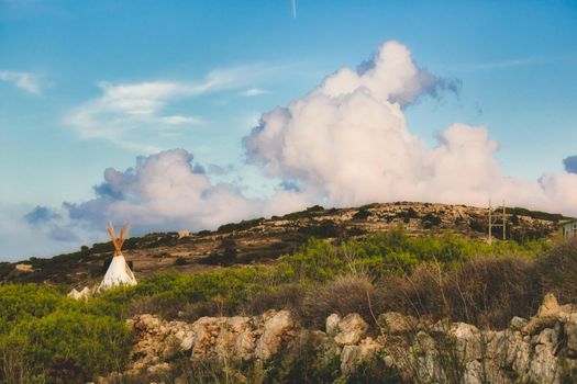 White canvas teepee (or wigwam) camped in a field under a cloudy blue sky
