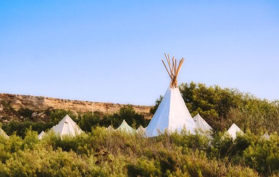 White canvas teepees (or wigwams) camped in a field under a clear blue sky