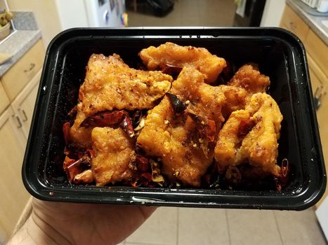 asian spicy fried Chinese fish with peppers in container in kitchen