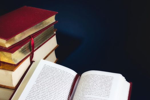 Stack of old books and an open book against a dark blue background with copy space for custom text