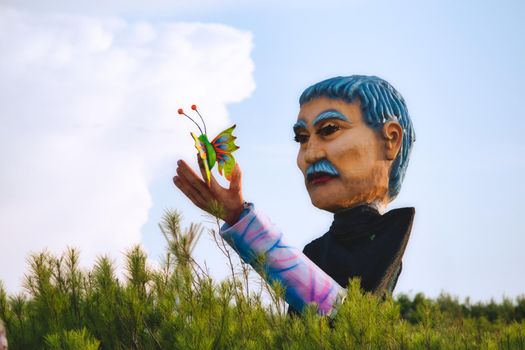 Giant fibre glass statue of a man holding a colorful butterfly outdoors in a field