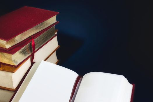 Stack of old books and an open book with blank empty pages against a dark blue background with copy space for custom text