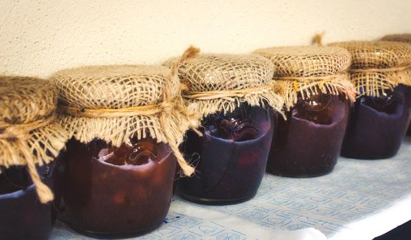 Glass jars of varied jams covered with sackcloth and tied with string in a row on a shelf