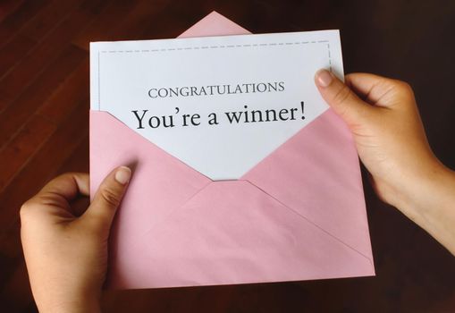 A letter that says Congratulations You're a winner! with female hands holding the open pink envelope