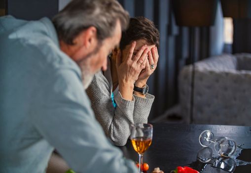 aged couple in the kitchen talking about something while drinking wine