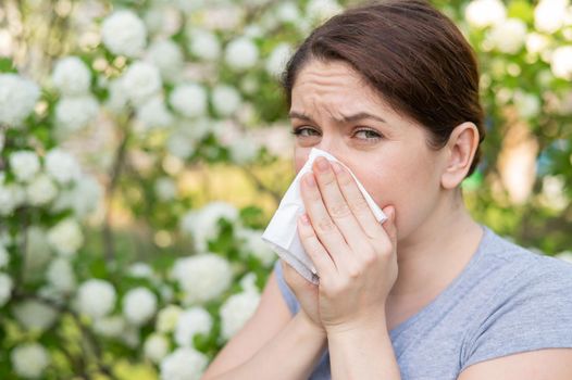 Caucasian woman suffers from allergies and sneezes while walking in the park