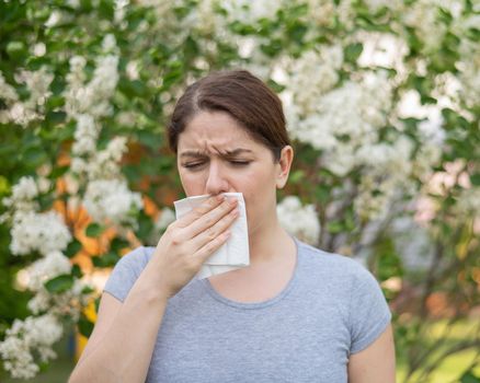 Caucasian woman suffers from allergies and blows her nose into a napkin while walking in the park