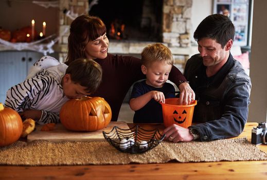 Shot of an adorable young family carving out pumpkins and celebrating halloween together at home.