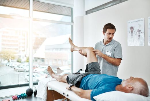 Shot of a young male physiotherapist helping a client with leg exercises whos lying on a bed.