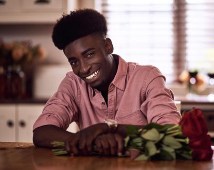 Cropped portrait of a handsome romantic young man smiling while holding a bunch of roses in his kitchen at home.