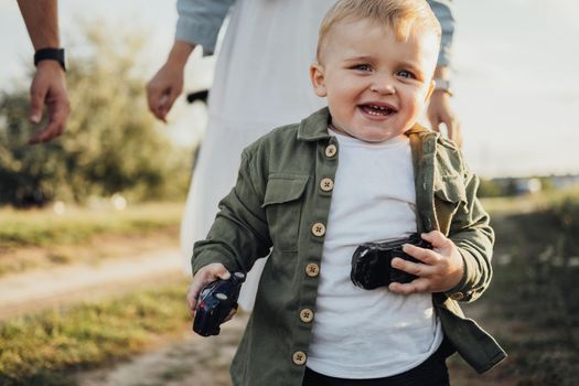 Funny Toddler Boy Holding Toys in Hands and Running Away from Parents Outdoors