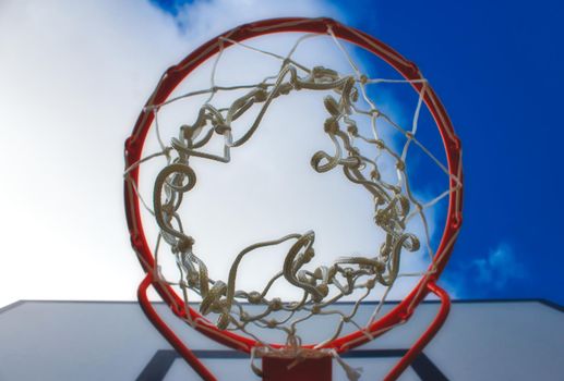 Close-up on basketball hoop looking up from below against a blue cloudy sky