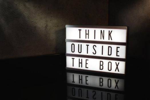 Think outside the box motivational message on a light box in a cinematic moody background