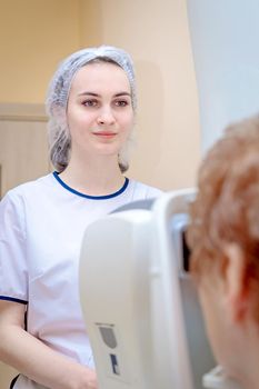 A girl optometrist examines the eyes of a patient using special modern equipment.