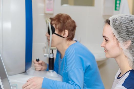 A girl optometrist examines the eyes of a patient using special modern equipment.
