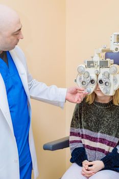 A male ophthalmologist checks a girl's eyesight using a phoropter. Vision treatment.