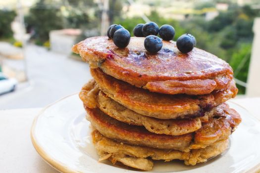 Big stack of homemade pancakes topped with blueberries and syrup