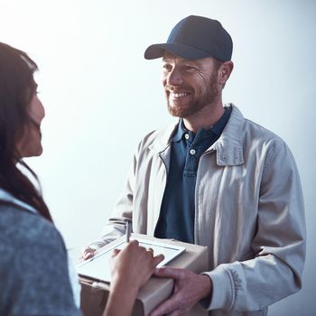 Shot of a cheerful delivery man handing over a package to a customer and letting them sign on a digital tablet inside a building.