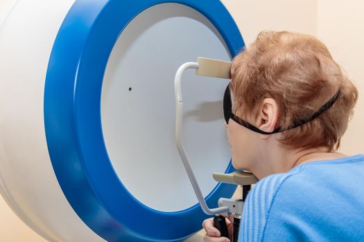 An adult girl at an ophthalmologist's appointment checks her eyesight on a special apparatus. Close-up.