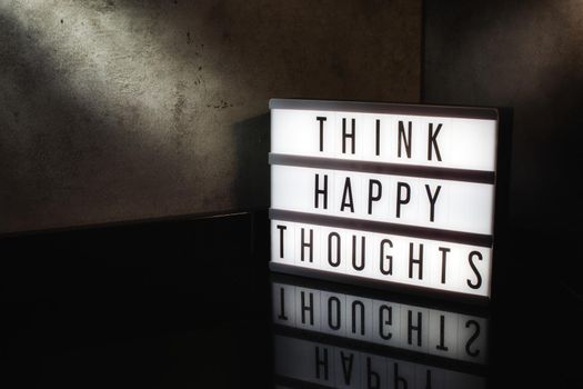 Think happy thoughts motivational message on a light box in a cinematic moody background