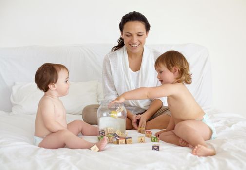 A young mother sitting in bed with her two babies busy putting wooden blocks in a jar.