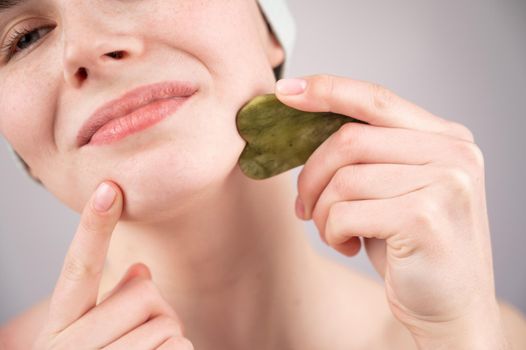 Close-up portrait of a young woman massaging her face with a gouache scraper