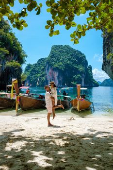 Koh Lao Lading near Koh Hong Krabi Thailand, beautiful beach with longtail boats, a couple of European men, and an Asian woman on the beach.