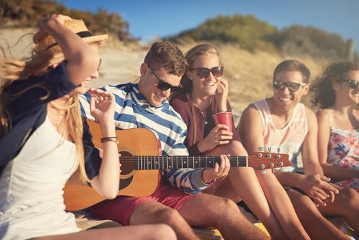Cropped shot of a handsome young man playing a guitar for his friends on a summers day at the beach.
