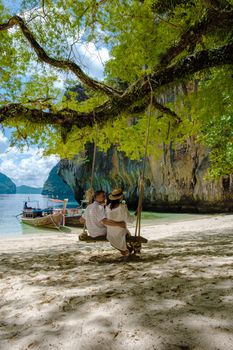 Koh Lao Lading near Koh Hong Krabi Thailand, beautiful beach with longtail boats, a couple of European men, and an Asian woman on the beach.