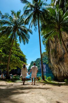 Koh Lao Lading near Koh Hong Krabi Thailand, beautiful beach with longtail boats, a couple of European men, and an Asian woman on the beach.