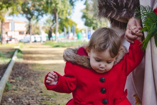 Little girl walking hand in hand with her mother on a path outdoors in a park in winter