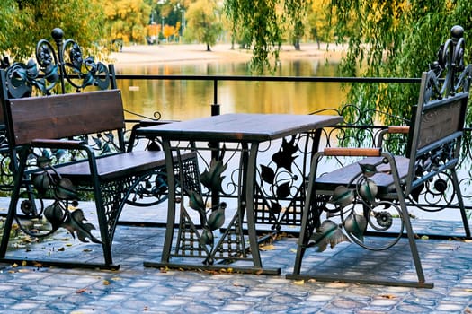 a small restaurant selling light meals and drinks. Two benches and a table made of carved metal and wood in a cafe on the shore of a clear lake. High quality photo