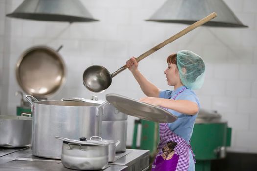 Cook prepares food. Cook with large pans and a ladle. Kitchen worker with a ladle. Chef professional