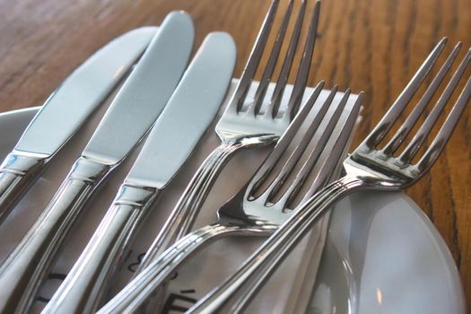 Shiny cutlery (knives and forks) and a ceramic plate on a table in a restaurant