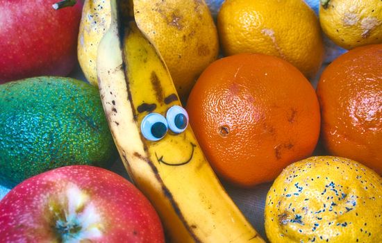 A bowl of fresh fruit with a smiley banana with a cheeky face drawn on