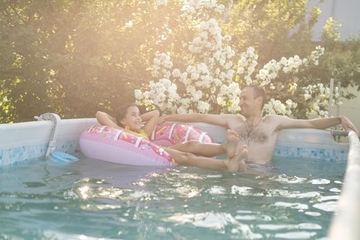 The father with little daughter have fun in the pool. Dad plays with the child. The family enjoy summer vacation in a swimming pool jumping, spinning, splash water