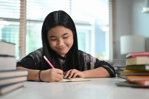 Smiling teenage girl doing homework at home.