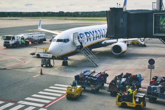 Gdansk / Poland - August 4 2019: Checked freight cargo luggage being driven towards a Ryanair aeroplane on the runway at Gdansk airport
