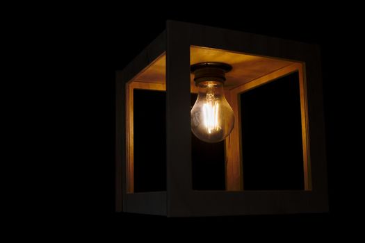 Warm yellow glowing light bulb encased in a wooden box against a black background