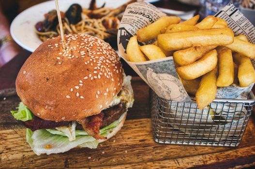 Burger and fries / chips in a basket on a wooden board in a restaurant