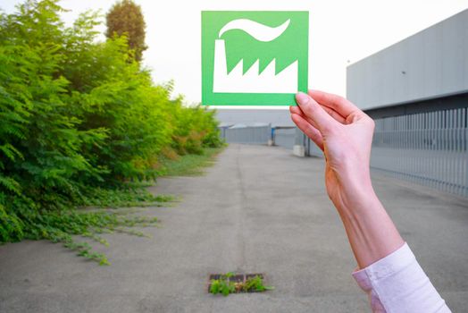 Hand holds green idustry symbol on industrial background.