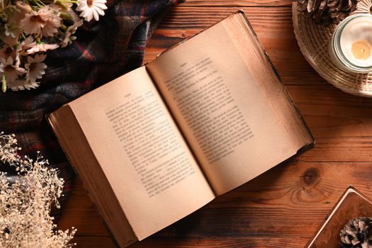 Old books, coffee cup, dried flowers and candles on a wooden table.