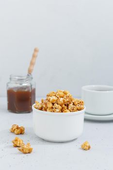 Sweet caramel popcorn in a ceramic bowl on a gray background with a jar of caramel and tea. Vertnical photo