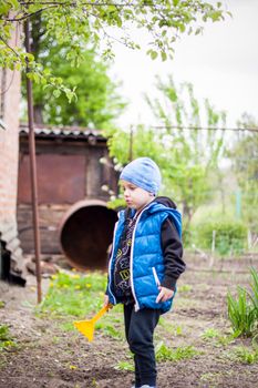 A child is planting a garden. A child's rake in his hands. A little gardener boy is planting plants in a flower bed. Gardening tools in the hands of a child. Garden, vegetable garden, children