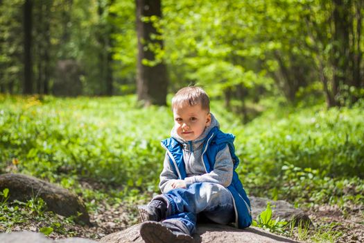 Portrait of a boy in a blue tank top in the woods in spring. Take a walk in the green park in the fresh air. The magical light from the sun's rays falls behind the boy. Spring