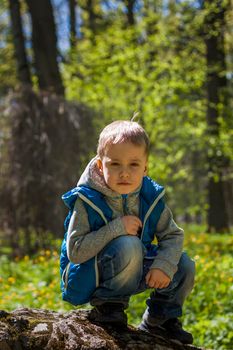 Portrait of a boy in a blue tank top in the woods in spring. Take a walk in the green park in the fresh air. The magical light from the sun's rays falls behind the boy. Spring