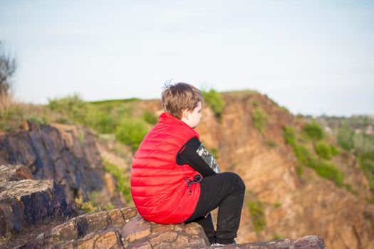 A child sits on top of a cliff and watches what is happening below. panoramic view from the top of a rocky mountain. Russia, Rostov region, skelevataya skala, the 7th wonder of the Don world. Landscape