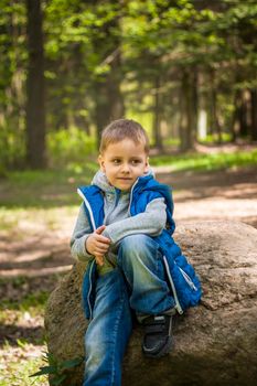 Portrait of a boy in a blue tank top in the woods in spring. Take a walk in the green park in the fresh air. The magical light from the sun's rays falls behind the boy. Spring