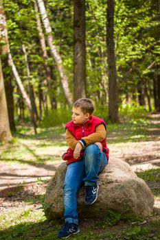 Portrait of a young man in a red tank top in the forest in spring. Walk through the green park in the fresh air. The magical light from the sun's rays falls behind the boy. Spring